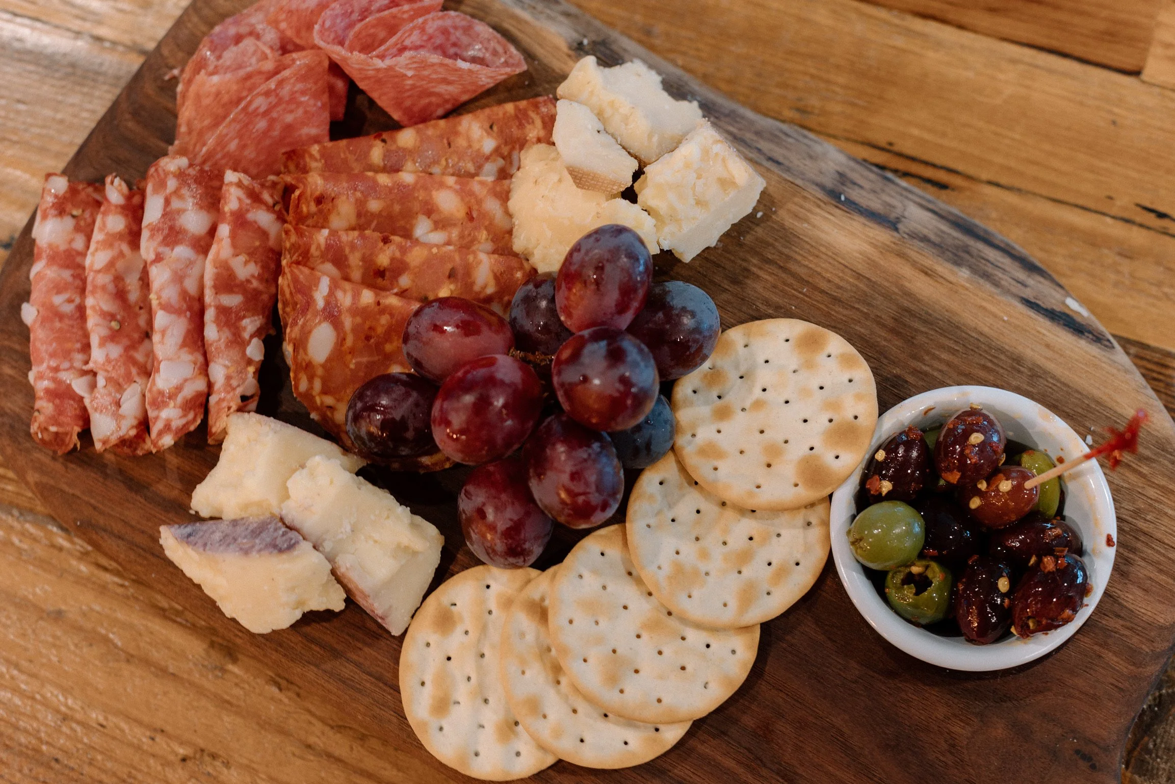 A charcuterie board with Italian meats, cheeses, grapes and olives